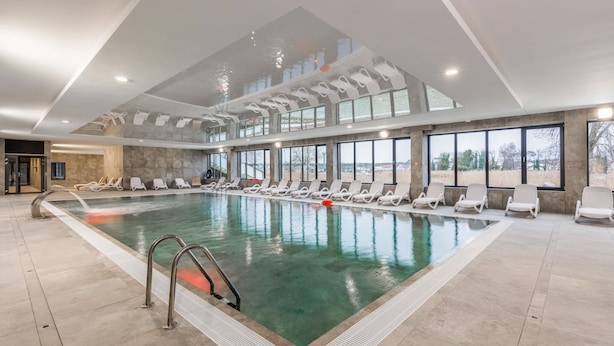 Una piscina interior con agua cristalina, rodeada de sillas de descanso y grandes ventanales con vistas al exterior.