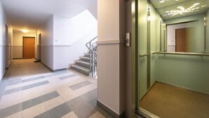 A hotel corridor with a staircase, a glass elevator, and a door at the end. - Cozy Studio in Downtown Sopot | Close to the Beach and the Pier (Sopot)