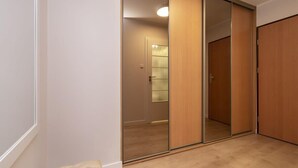 A room with a sliding door leading to a bathroom, a wooden floor, and a small tufted bench. - Cozy Studio in Downtown Sopot | Close to the Beach and the Pier (Sopot)