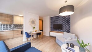 A modern living room with a sofa, a coffee table, and a dining area with chairs and a table. - Cozy Studio in Downtown Sopot | Close to the Beach and the Pier (Sopot)
