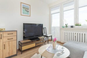 Uma sala de estar moderna com televisão de tela plana, armário de madeira, mesa de centro redonda e uma janela com persianas.