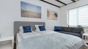 A bedroom with a large bed, two bedside tables, a grey sofa, and two wall-mounted paintings.