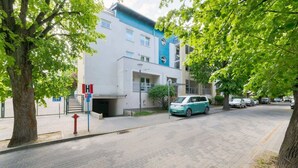 Ein modernes Gebäude mit blau-weißer Fassade, einem gut sichtbaren Eingang und einer gepflasterten Straße mit parkenden Autos.
