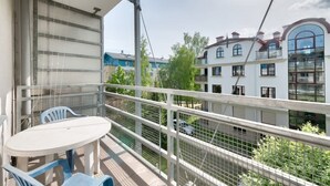 Ein Balkon mit Tisch und Stühlen, Blick auf benachbarte Gebäude und einem Metallgeländer.
