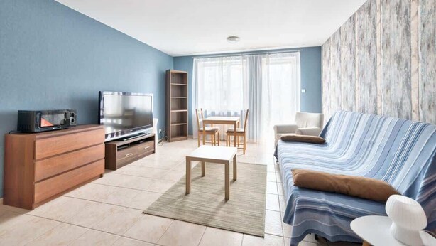 Ein modernes Wohnzimmer mit Sofa, Fernseher, Holzschrank und einem Essbereich mit Stühlen und Tisch.