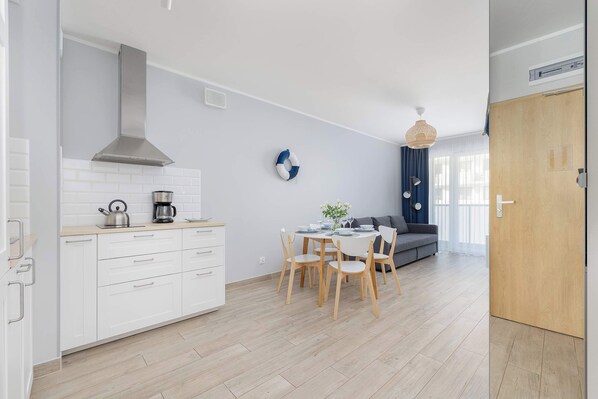A modern kitchen with white cabinets, a stainless steel range hood, and a dining area with a round table and chairs.