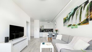 A modern living room with a flat-screen TV, a sofa, a coffee table, and a dining area with chairs and a table.