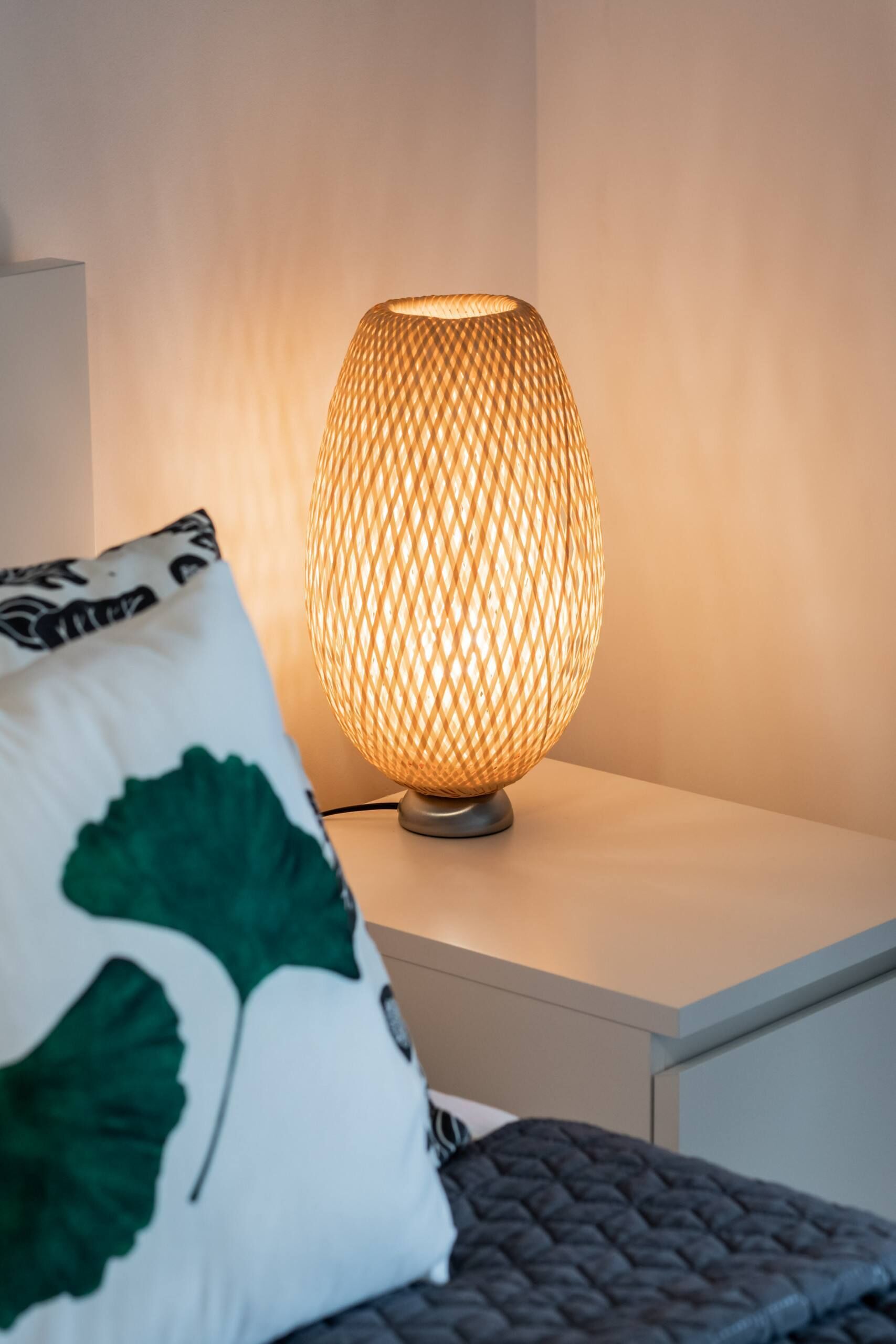 Eine Nachttischlampe mit Gewebemuster auf einem Nachttisch.