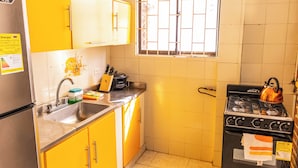 A kitchen with yellow cabinets, a stainless steel sink, a stove, and a window with bars. - Casa del parque  (Cartagena)