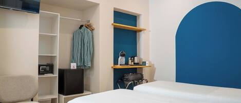 A hotel room with a bed, a TV, a wardrobe, a chair, and a desk with a kettle and coffee maker.