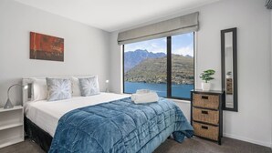A bedroom with a large bed, a view of mountains and water, a bedside table with a lamp, and a mirror on the wall. - Perfect Place To Stay! Views! (Queenstown)