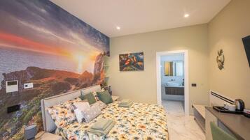 Een slaapkamer met een grote muurschildering van een zonsondergang, een bed met bloemenbeddengoed en een badkamer die door een open deur zichtbaar is.
