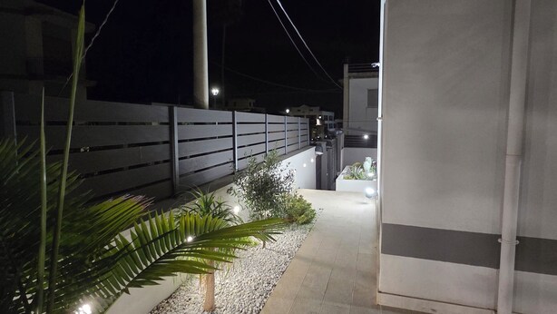 A nighttime outdoor pathway with a railing, potted plants, and a building entrance.