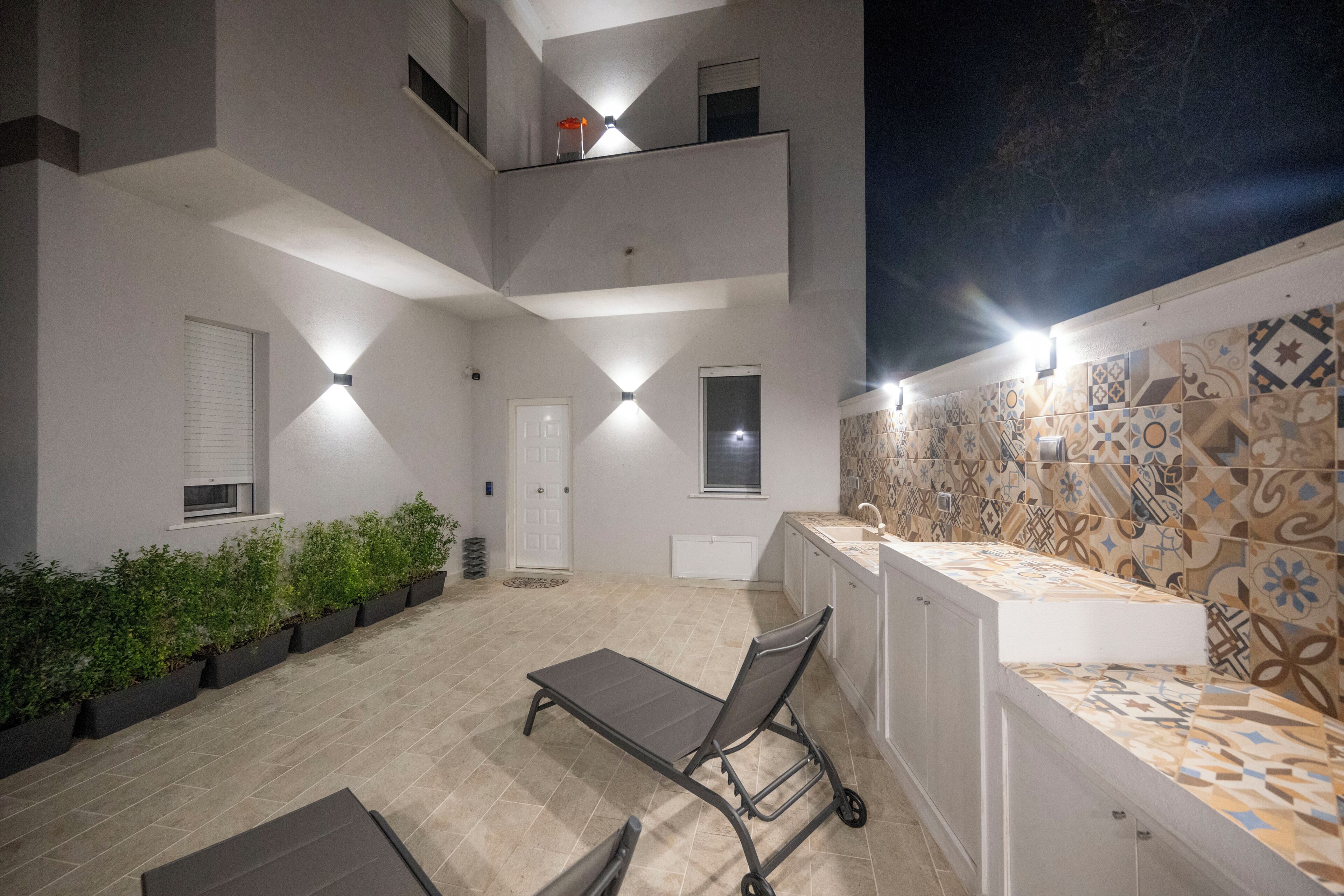 A multi-level outdoor area with a dining table and chairs, a small balcony, and patterned tile walls.
