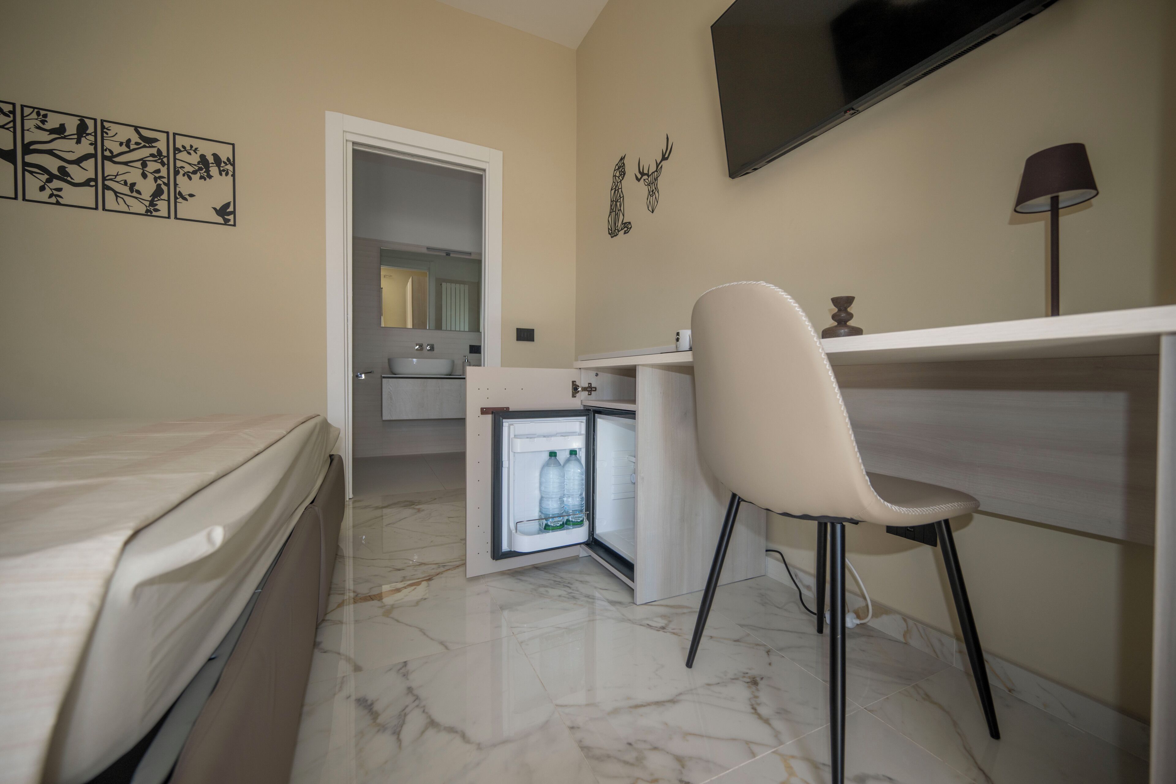 Ein kleines Hotelzimmer mit Bett, Schreibtisch, Stuhl, Fernseher und einem kleinen Kühlschrank.