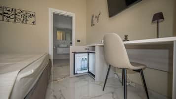 Ein kleines Hotelzimmer mit Bett, Schreibtisch, Stuhl, Fernseher und einem kleinen Kühlschrank.