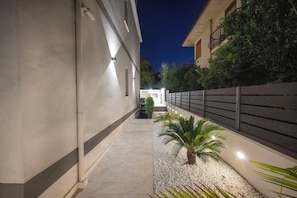 A nighttime corridor with a pathway, a palm tree, and a building with a balcony. - Exclusive B&B Villa Rosa (Messina)