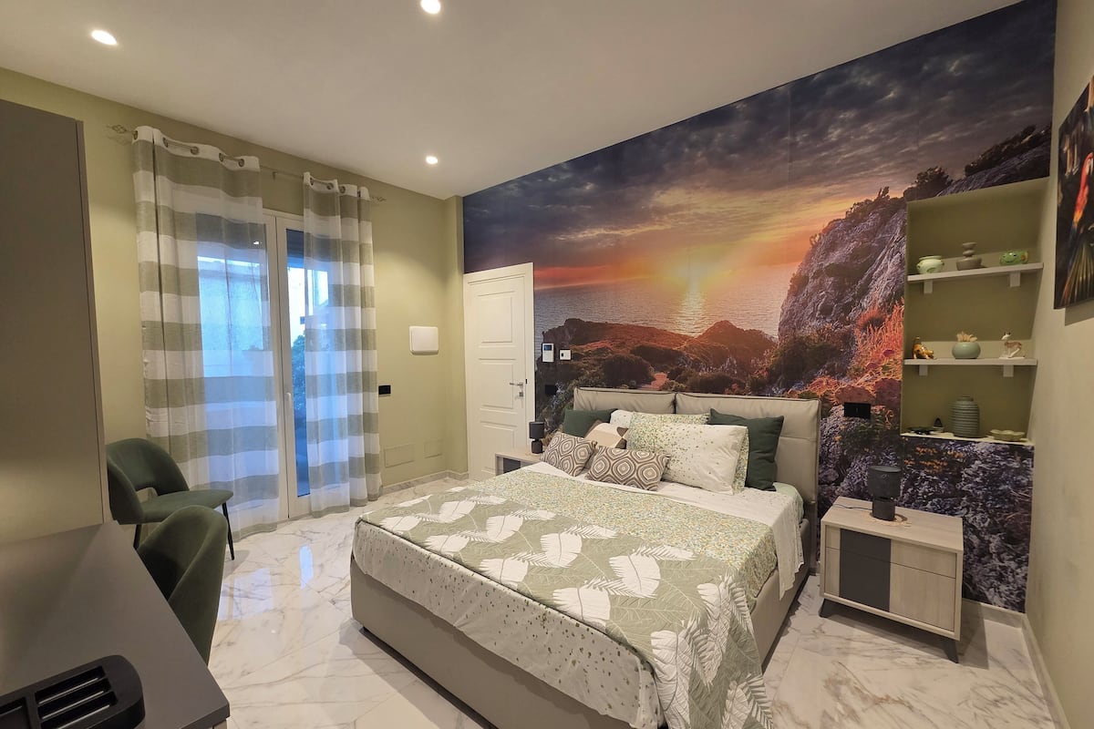 Un dormitorio con cama, escritorio, silla, mesita de noche y estante con objetos decorativos.