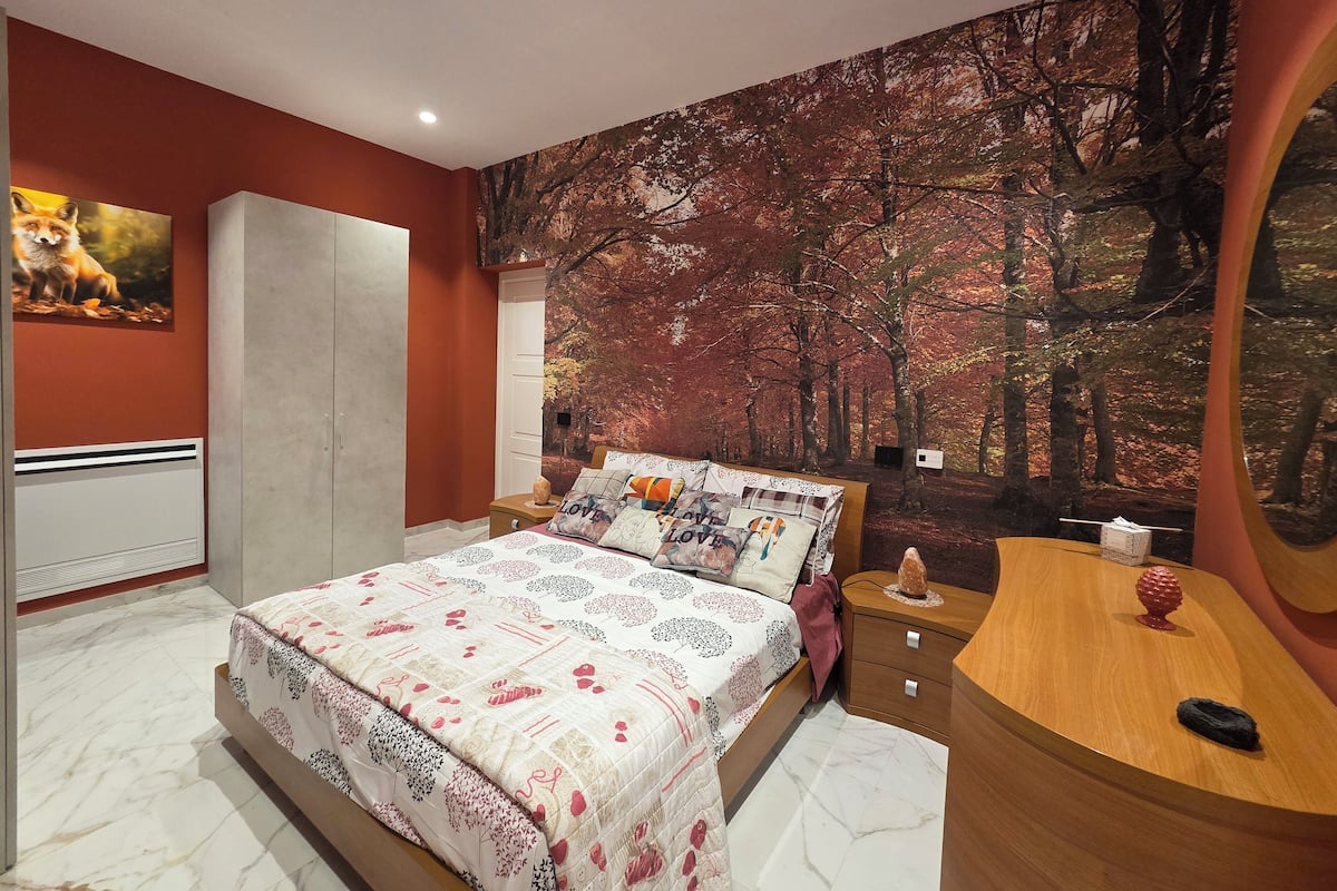 Un dormitorio con cama, mesita de noche, cómoda y un gran mural con motivos forestales en la pared.