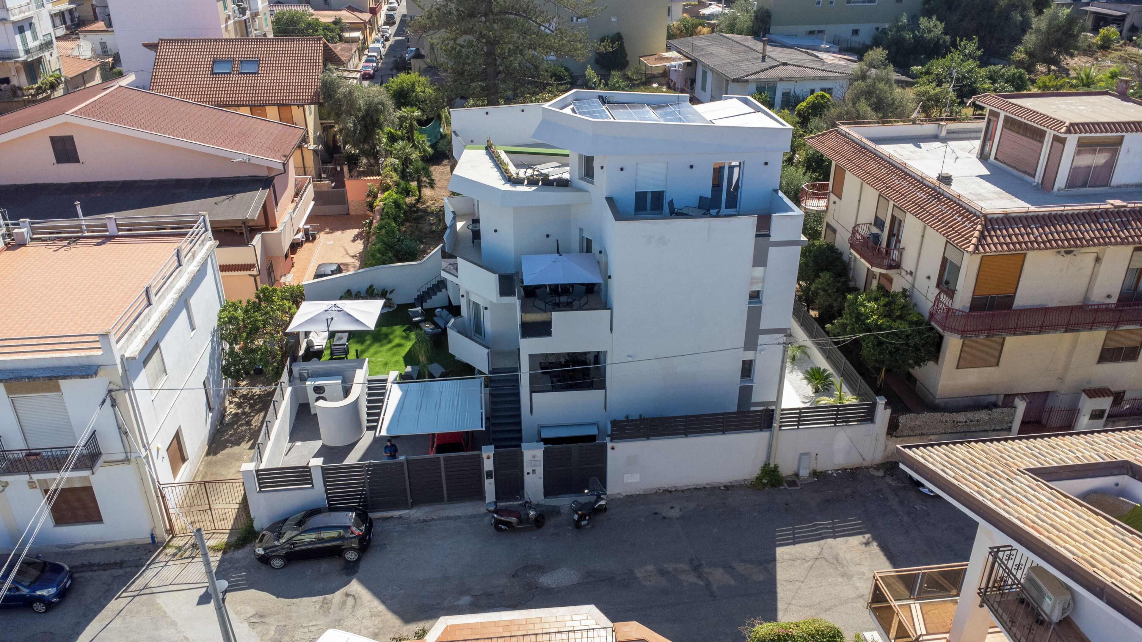 A multi-story residential building with a flat roof, solar panels, and a gated entrance.