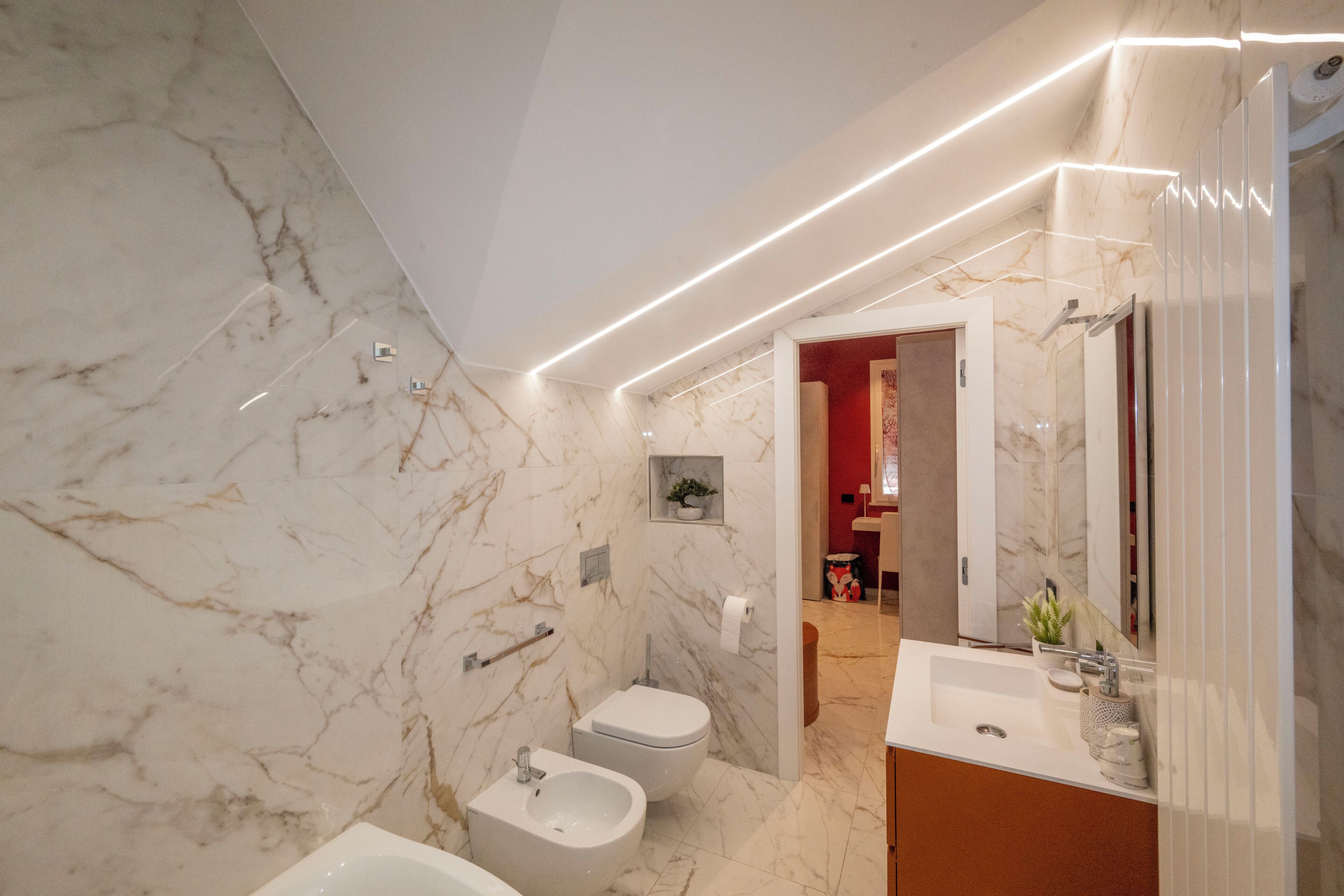 Een moderne badkamer met een marmeren wand, een bidet, toilet en een wastafel met spiegel.