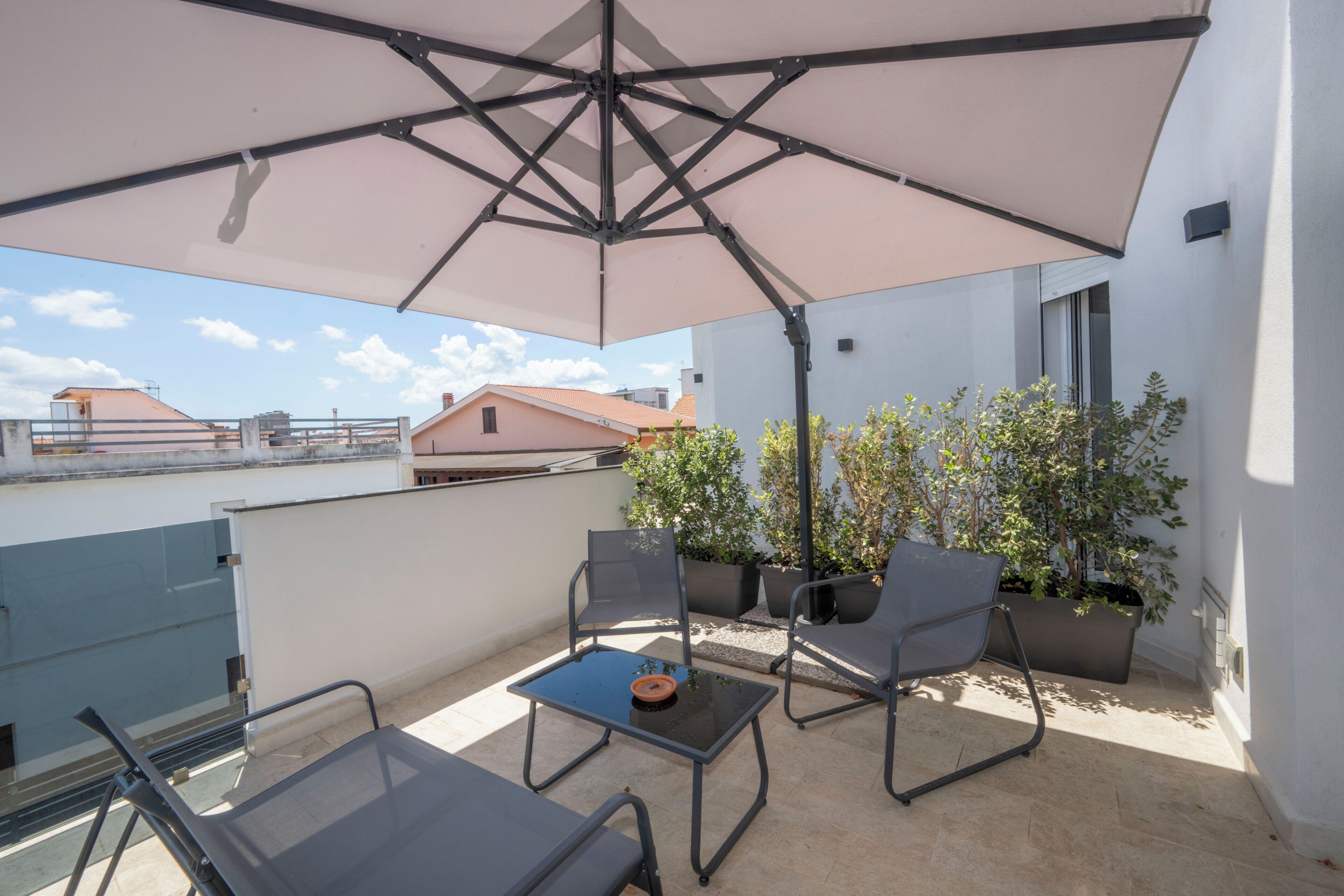 Una terraza en la azotea con una mesa, sillas, una sombrilla y plantas en macetas.