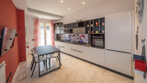 A modern kitchen with a dining area, featuring a marble floor, built-in appliances, and decorative items on shelves. - Exclusive B&B Villa Rosa (Messina)