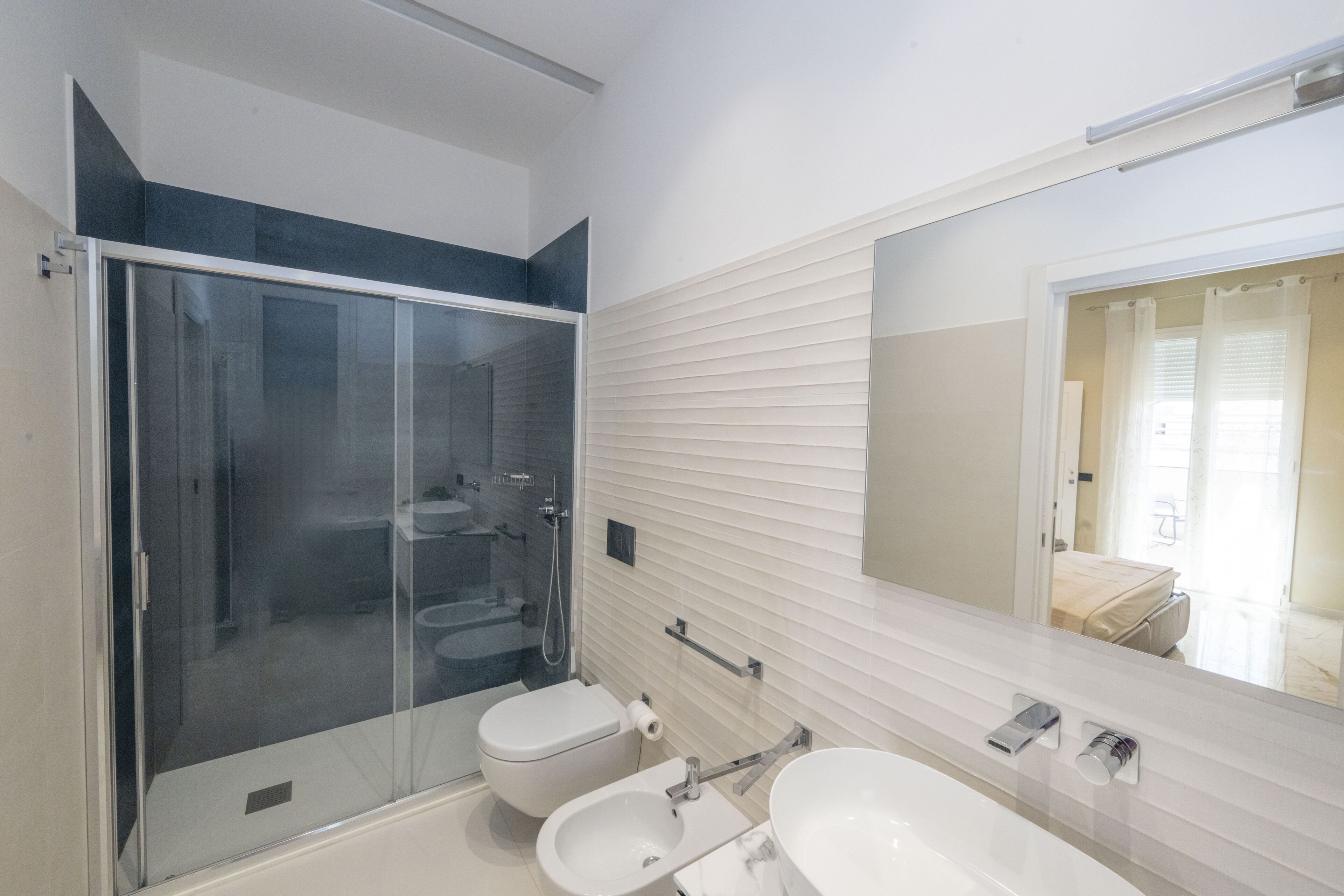 Un baño moderno con cabina de ducha de vidrio, inodoro, bidé y un espejo grande.