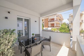 Un balcón con puerta de vidrio, una mesa con sillas y una planta en maceta.