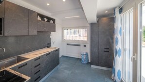 A modern kitchen with dark marble countertops, a built-in oven, and a window with patterned curtains. - Exclusive B&B Villa Rosa (Messina)