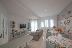 Una sala moderna con un sofá, una mesa de comedor y un televisor montado en la pared.