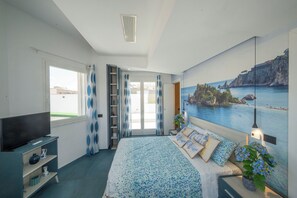Un dormitorio con una cama, un televisor, una ventana y un cuadro de una escena costera.