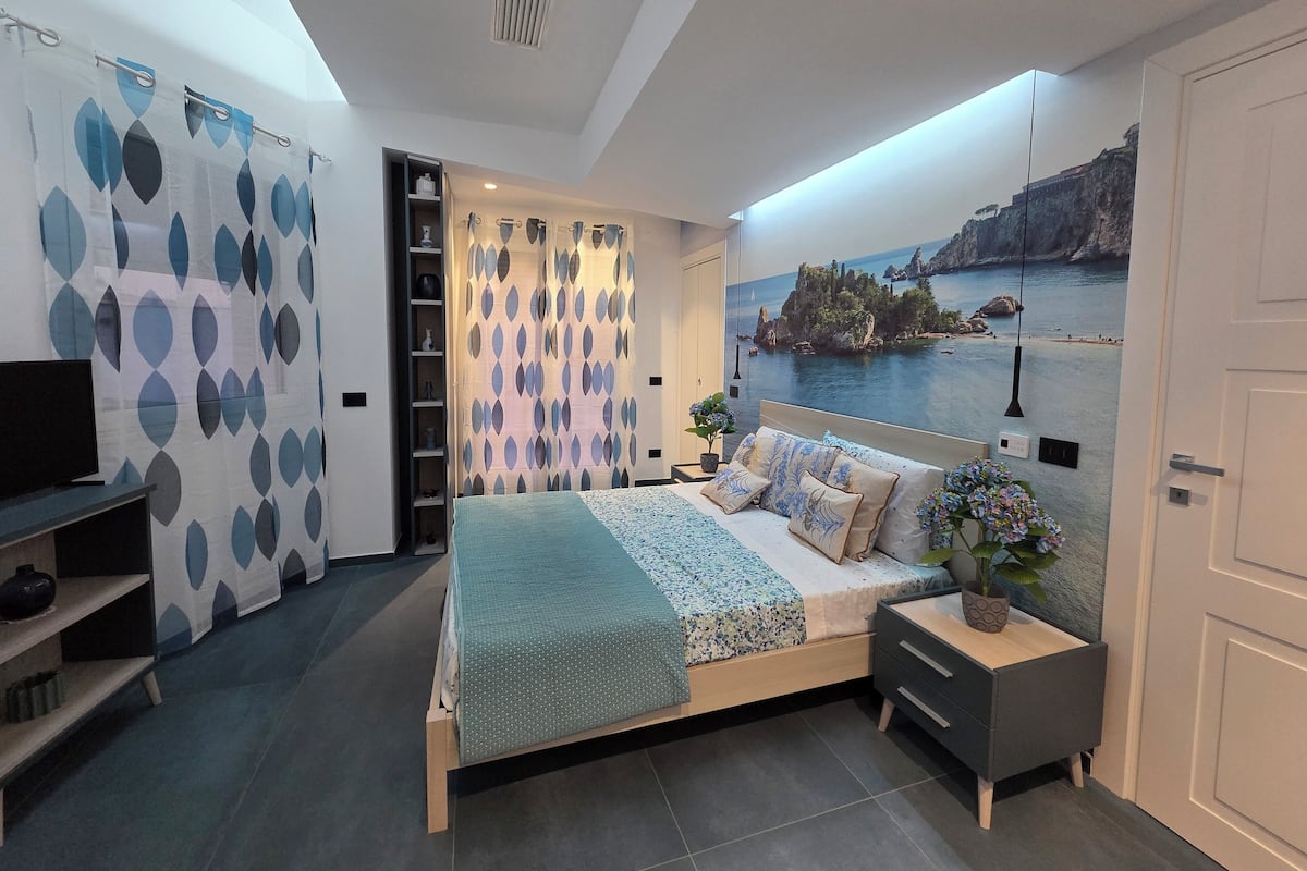 Un dormitorio moderno con cama, mesita de noche y un amplio ventanal con vistas panorámicas.
