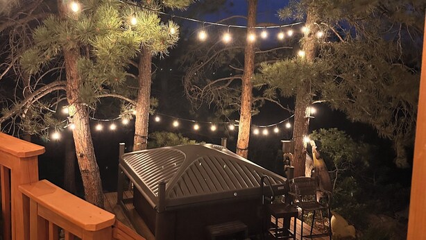Une terrasse dotée d’un jacuzzi, entourée d’arbres et illuminée de guirlandes lumineuses.