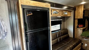 Un intérieur de camping-car compact avec un réfrigérateur noir, un banc en bois et un coin cuisine.