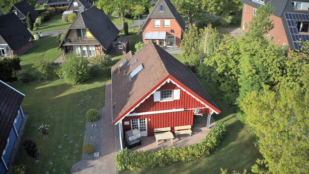 A red house with a sloped roof, a covered porch, and a small garden area. - Vacation home Seerose am Elbdeich in Otterndorf (Otterndorf)