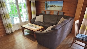A cozy living room with a wooden floor, a grey sofa with cushions, a wooden coffee table, and a television mounted on the wall. - Vacation home Seerose am Elbdeich in Otterndorf (Otterndorf)
