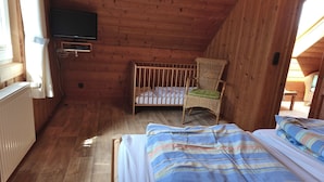 A cozy cabin room with a wooden floor, a crib, a wicker chair, and a bed with striped bedding. - Vacation home Seerose am Elbdeich in Otterndorf (Otterndorf)