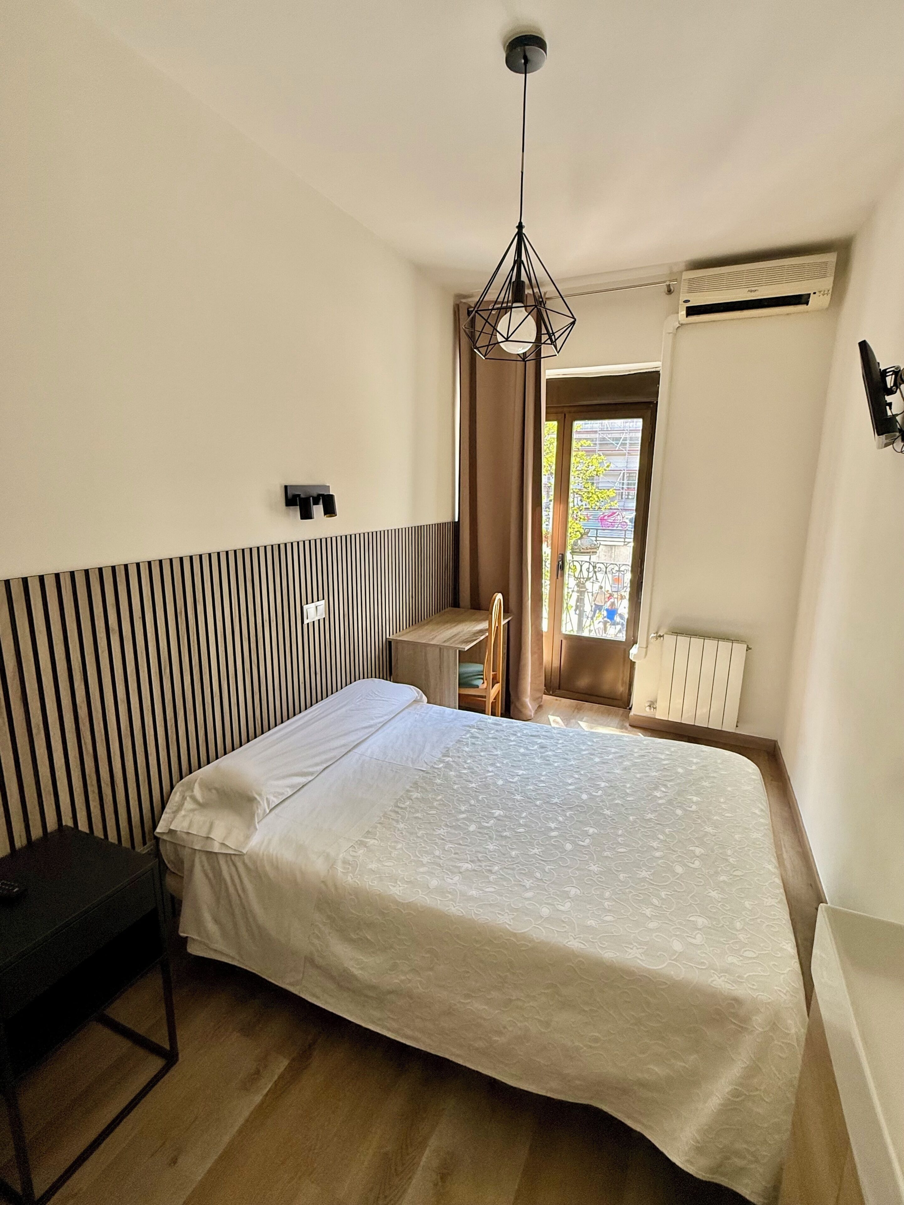 Una camera da letto con un letto, una scrivania, una sedia, un termosifone e una finestra vista esterna.