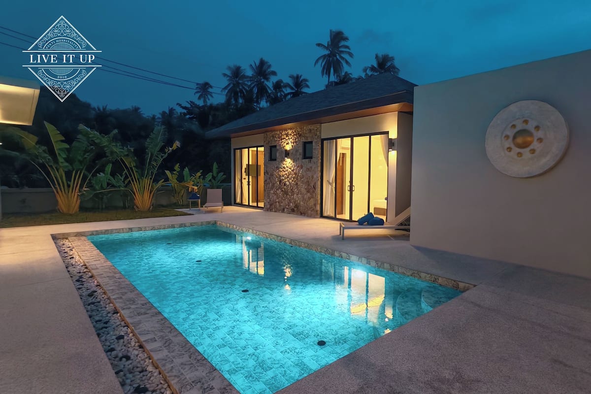 A modern house with a swimming pool, stone walls, and a well-lit entrance.