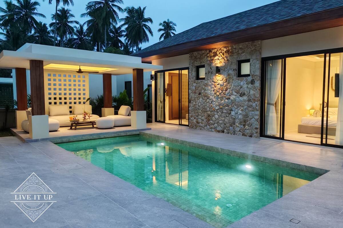 A modern pool area with a stone wall and a glass door leading to a bedroom.