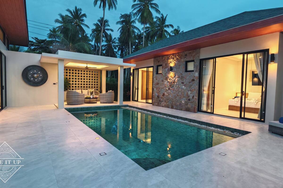 A modern pool area with a stone wall and a bedroom visible through a glass door.