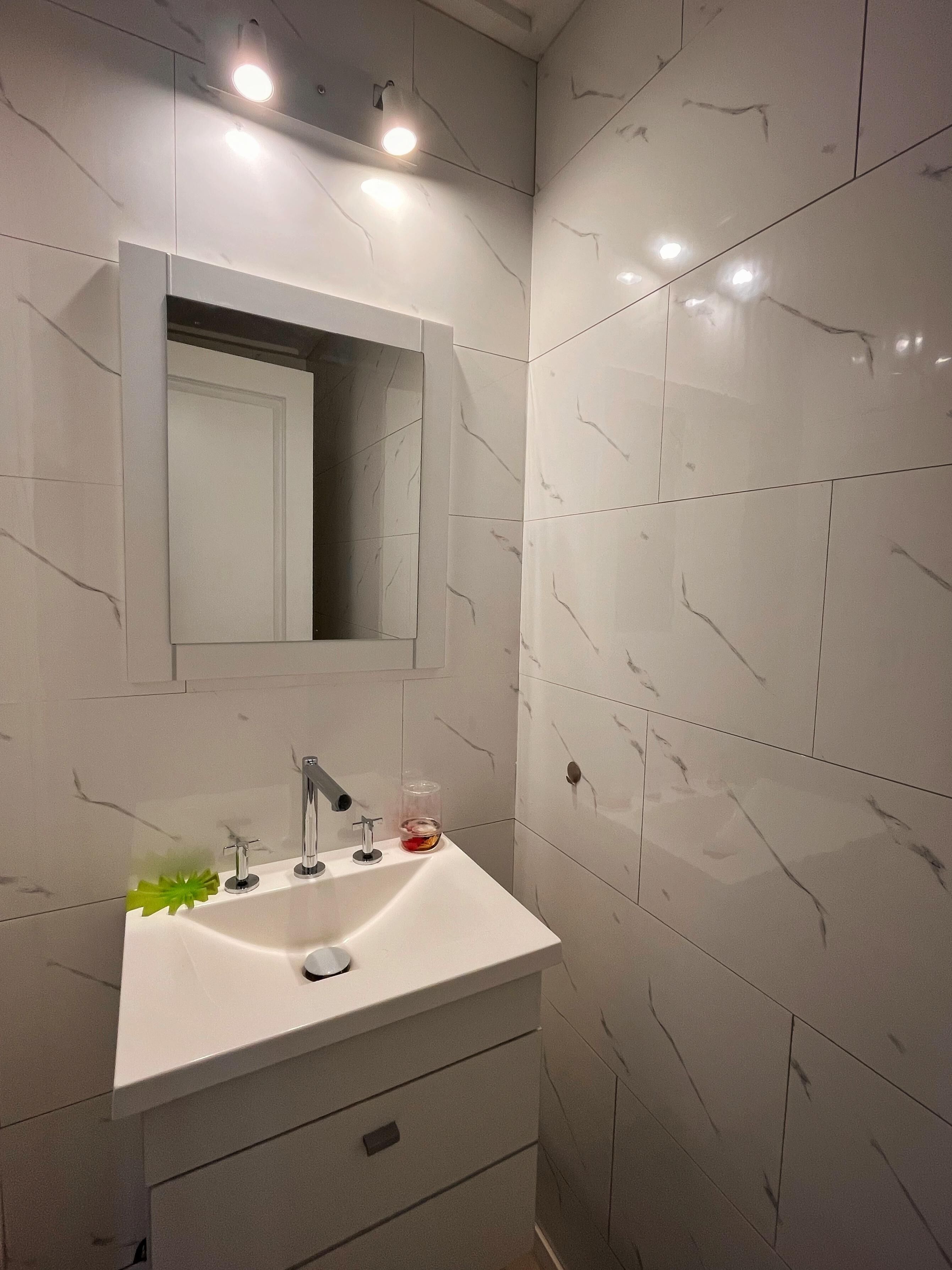 A bathroom with a white sink, a mirror, and a light fixture above the mirror.