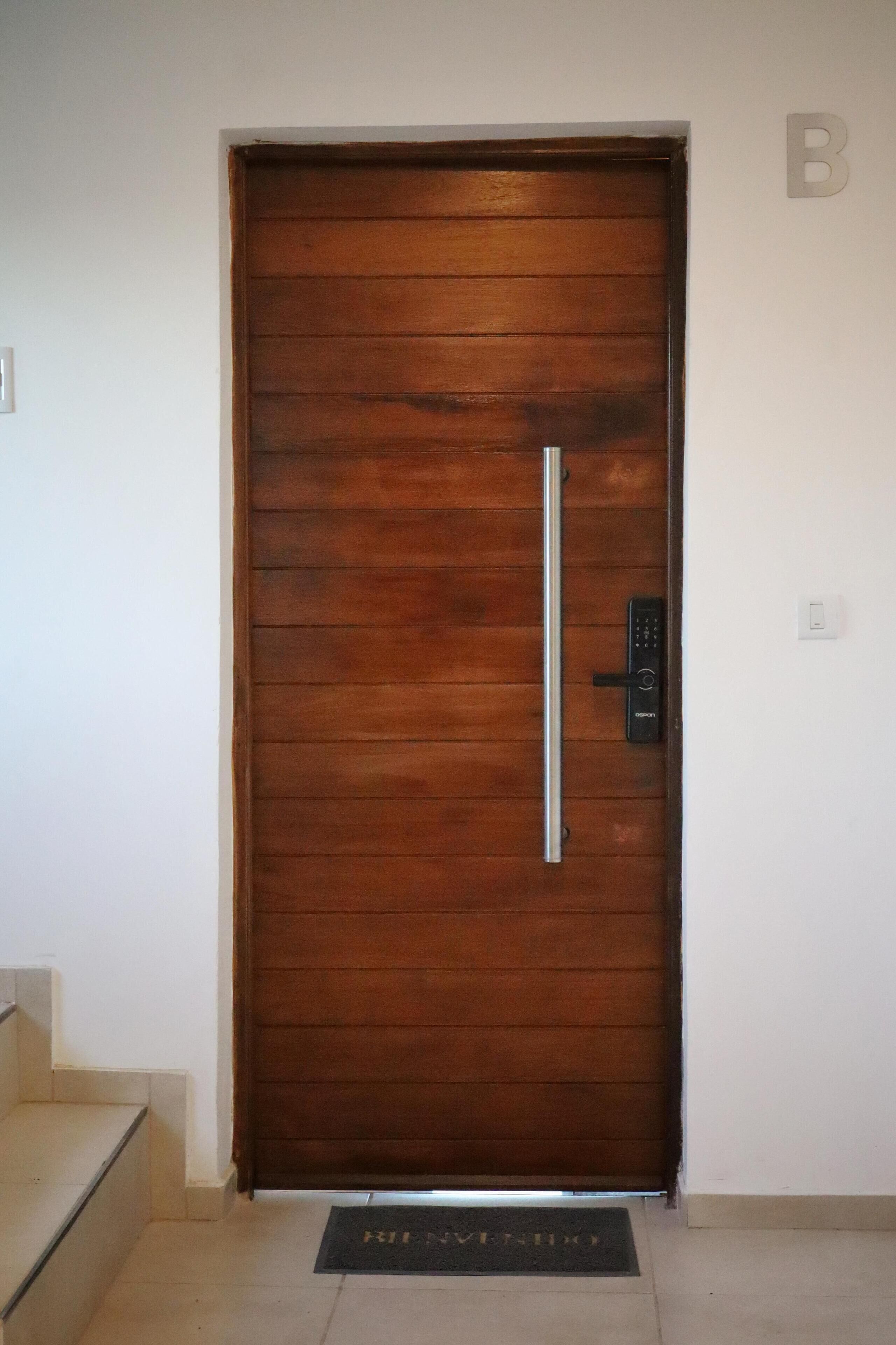 Una puerta de madera con manija vertical y cerradura electrónica.