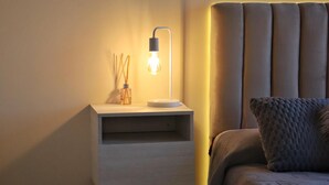 Un dormitorio ordenado con una mesita de noche, una lámpara y una cama con cabecero.