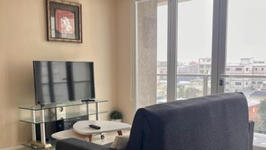 Una sala de estar moderna con un ventanal grande, un televisor de pantalla plana, una mesa de centro de vidrio y un sofá gris.