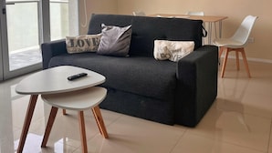 Una sala moderna con un sofá gris, una mesa de centro blanca y un comedor con una mesa y sillas blancas.