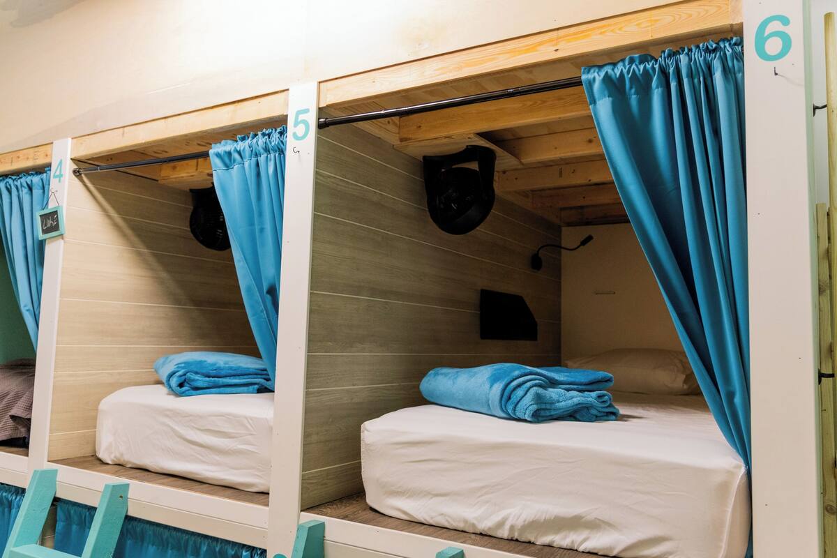 A bunk bed room with numbers 4, 5, and 6, wooden walls, and blue curtains.