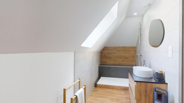 A modern bathroom with a skylight, a wooden vanity, a white sink, and a mirror.