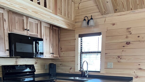 A kitchen with wooden cabinetry, a black stove, a microwave, and a sink.